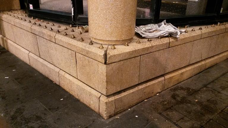 Eine Ecke von einem Gebäude in London, auf der viele kleine Metallspitzen angebracht sind. 