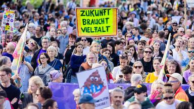 Mehrere Menschen auf einer Demo, eine Teilnehmerin hält ein Schild mit der Aufschrift "Zukunft braucht Vielfalt"