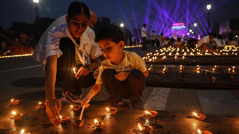 Ein Junge und eine erwachsene Frau zünden beim Diwali-Fest Lichter an.