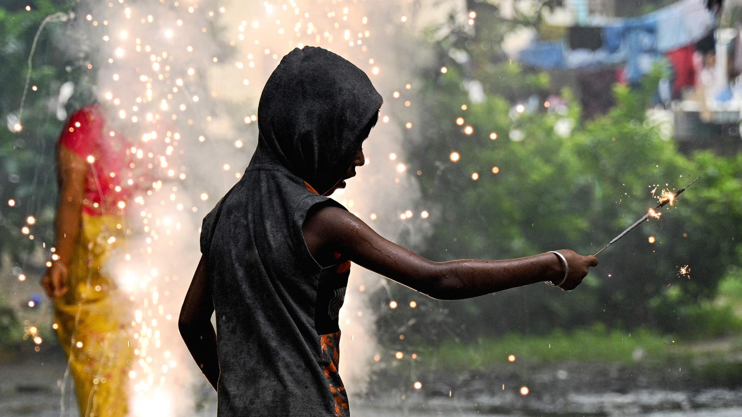 Ein Junge zündet während Diwali-Feierlichkeiten eine Wunderkerze an, im Hintergrund sprühen Funken.