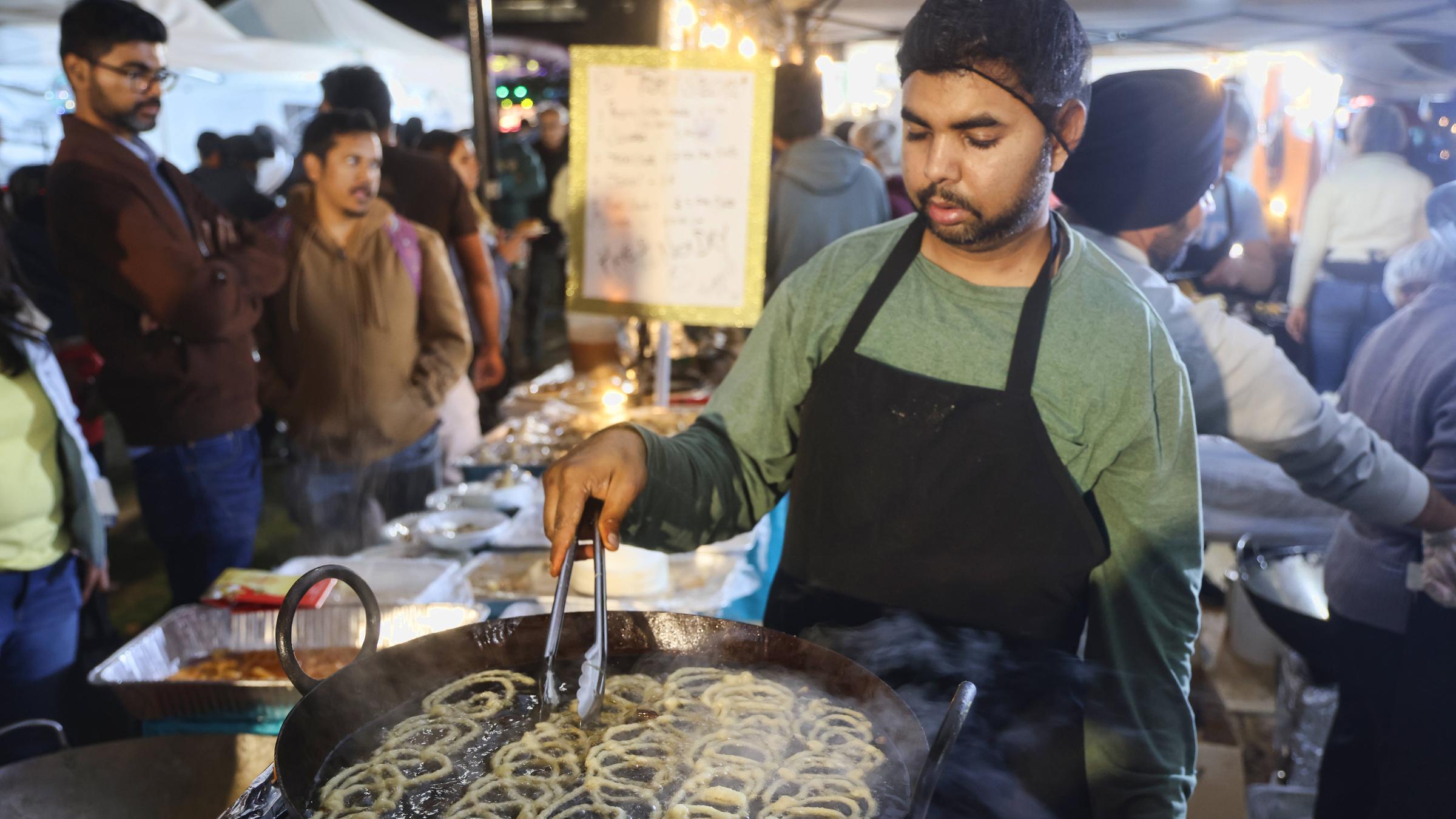 Ein Mann frittiert helle Kringel aus Teig in einer großen Pfanne.