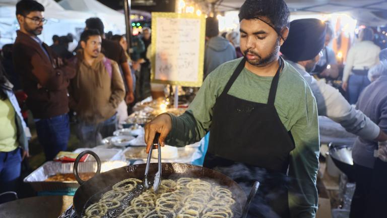 Ein Mann frittiert helle Kringel aus Teig in einer großen Pfanne.