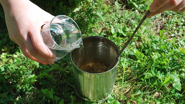 Es wird Wasser zur Erde hinzugekippt, um Lehm anzumischen