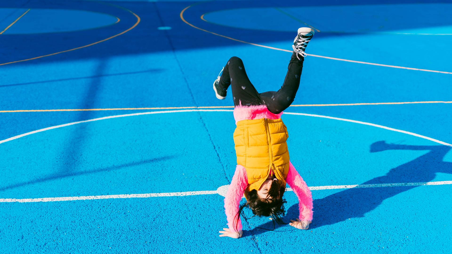 Ein Mädchen macht einen Handstand auf einem Sportplatz. 