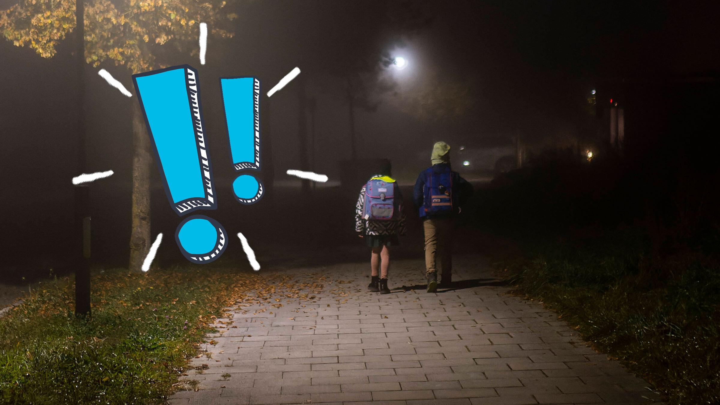 Zwei Schulkinder laufen nebeneinander im Dunkeln zur Schule, daneben zwei blaue Ausrufezeichen.