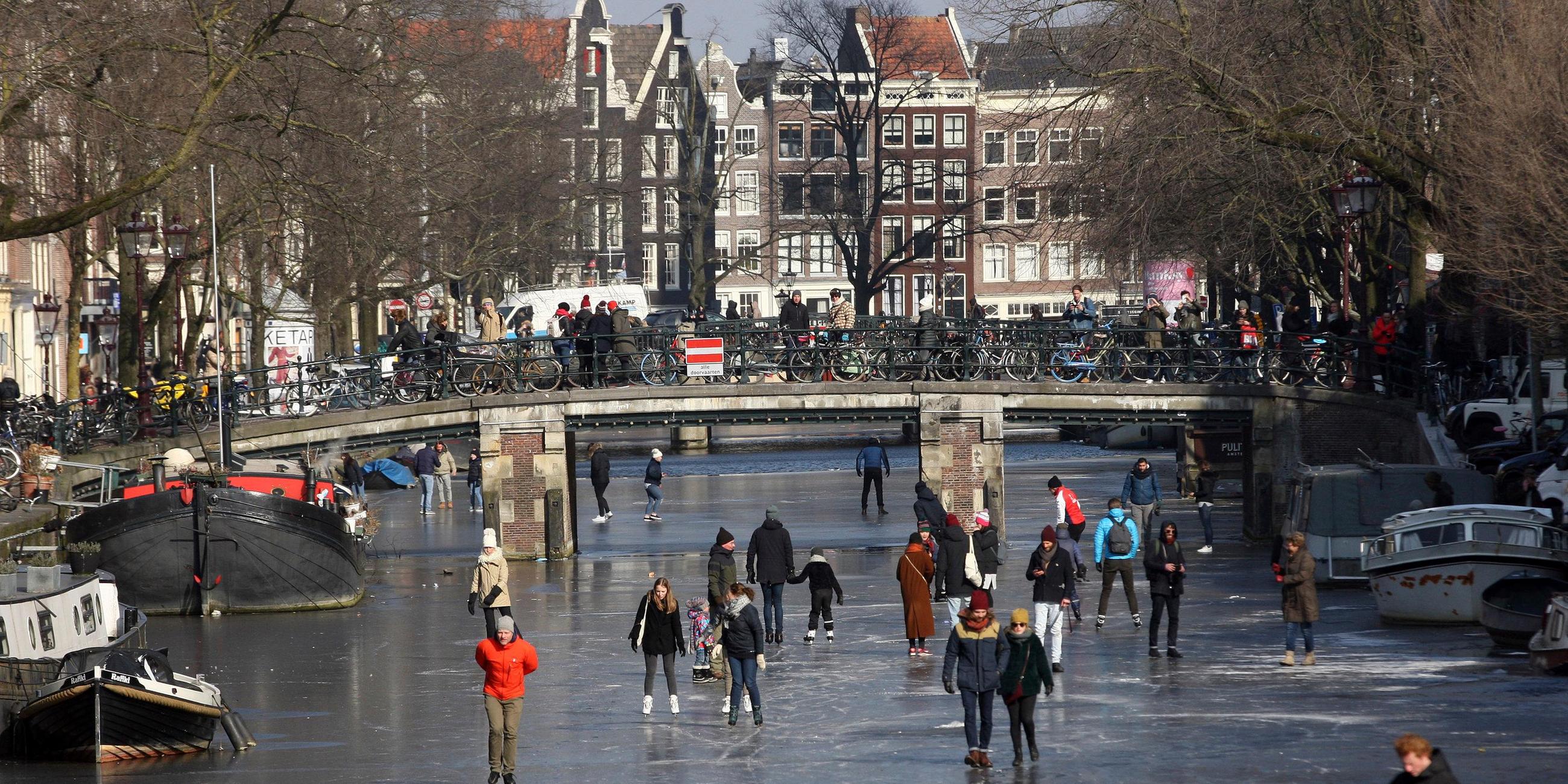 Menschen gehen auf den Kanälen in Amsterdam Eislaufen.