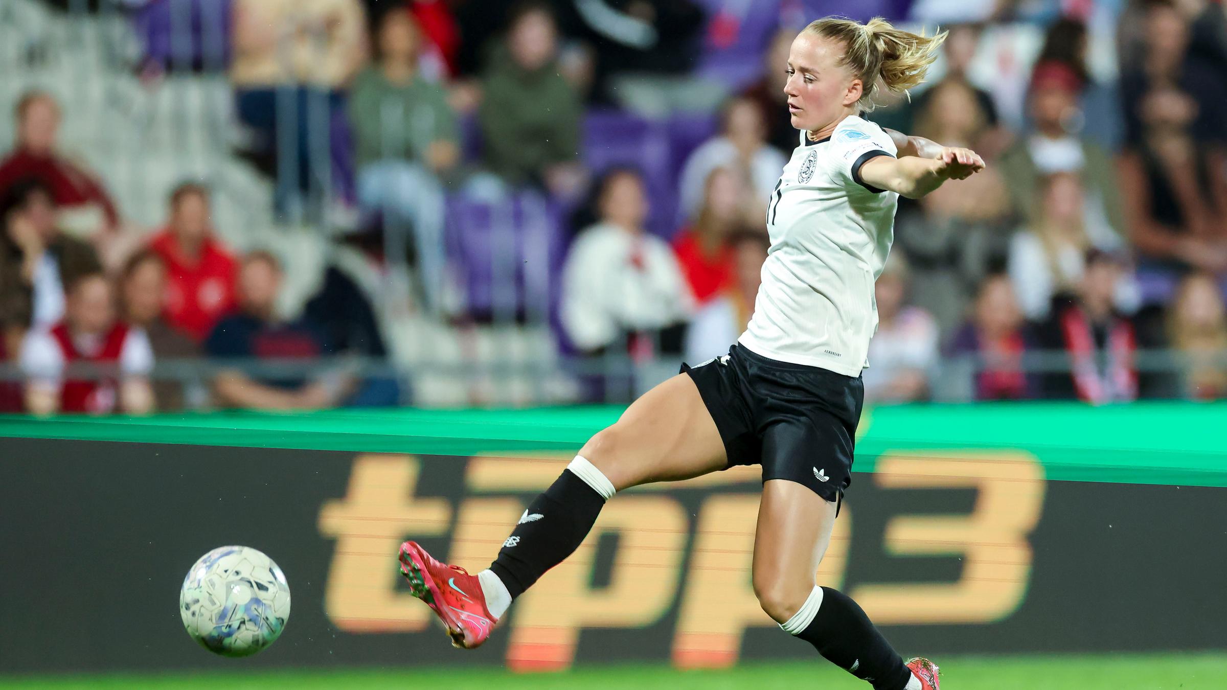 Lea Schueller hat die Arme ausgebreitet und schaut auf den Ball zu ihren Füßen auf dem Fußballplatz