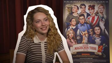 Schauspielerin Emilia Maier neben ihr das Plakat des neuen Kinofilms "Die Schule der magischen Tiere 4".