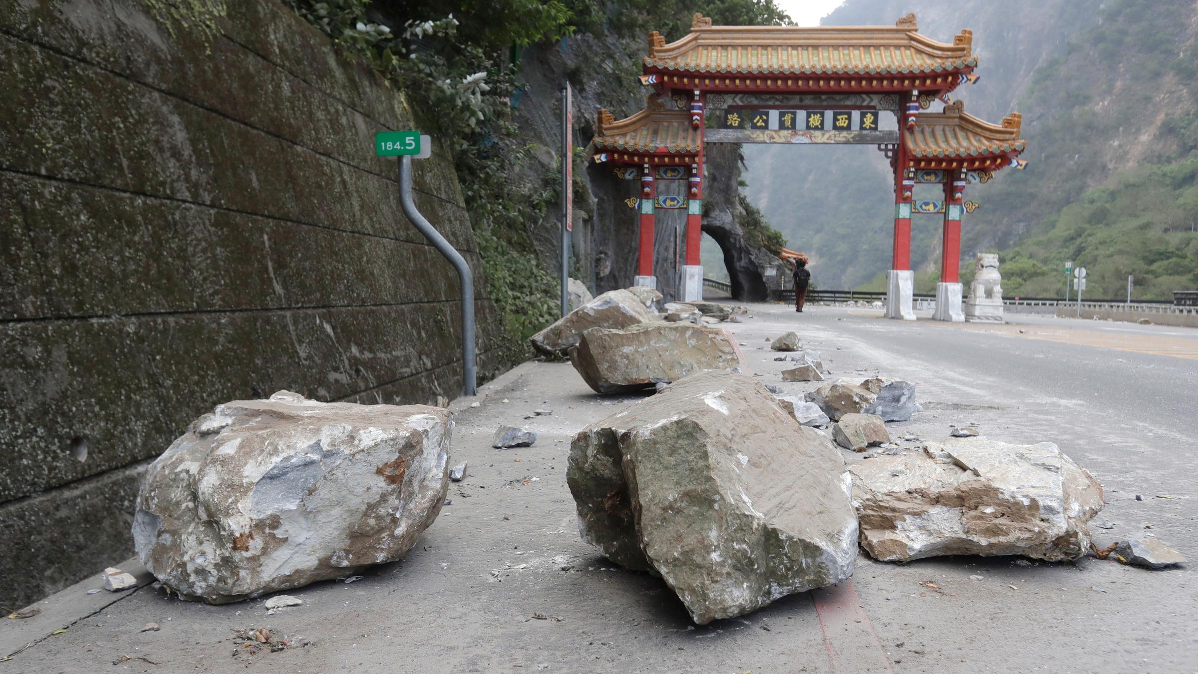 Riesige Felsbrocken liegen auf der Straße, im hintergrund ist eine Pagode zu sehen.