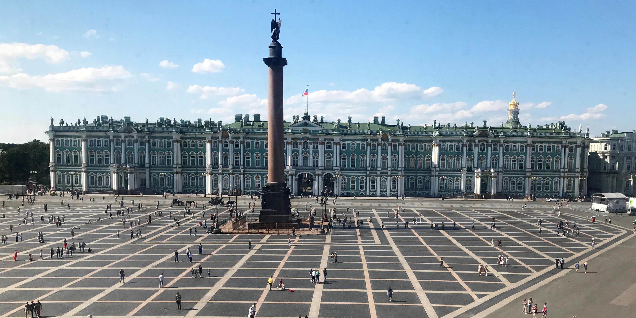 Man sieht das Kunstmusseum Eremitage und seinen Vorplatz, auf dem mehrere Menschen sind. 