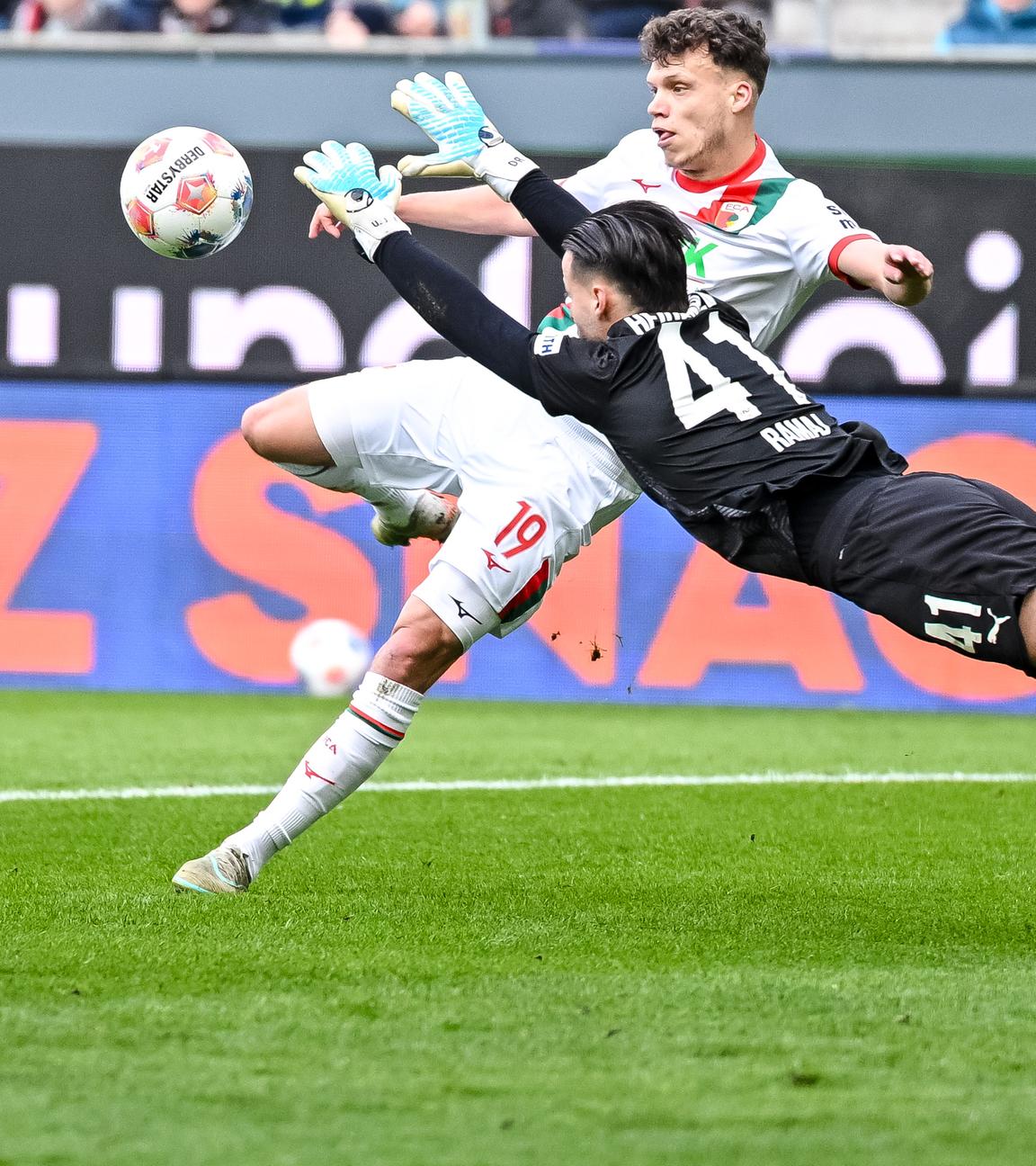 Augsburgs defensiver Mittelfeldspieler Robin Fellhauer versucht auf das Tor zu schießen, Heidenheims Torwart Diant Ramaj hechtet in Richtung Ball
