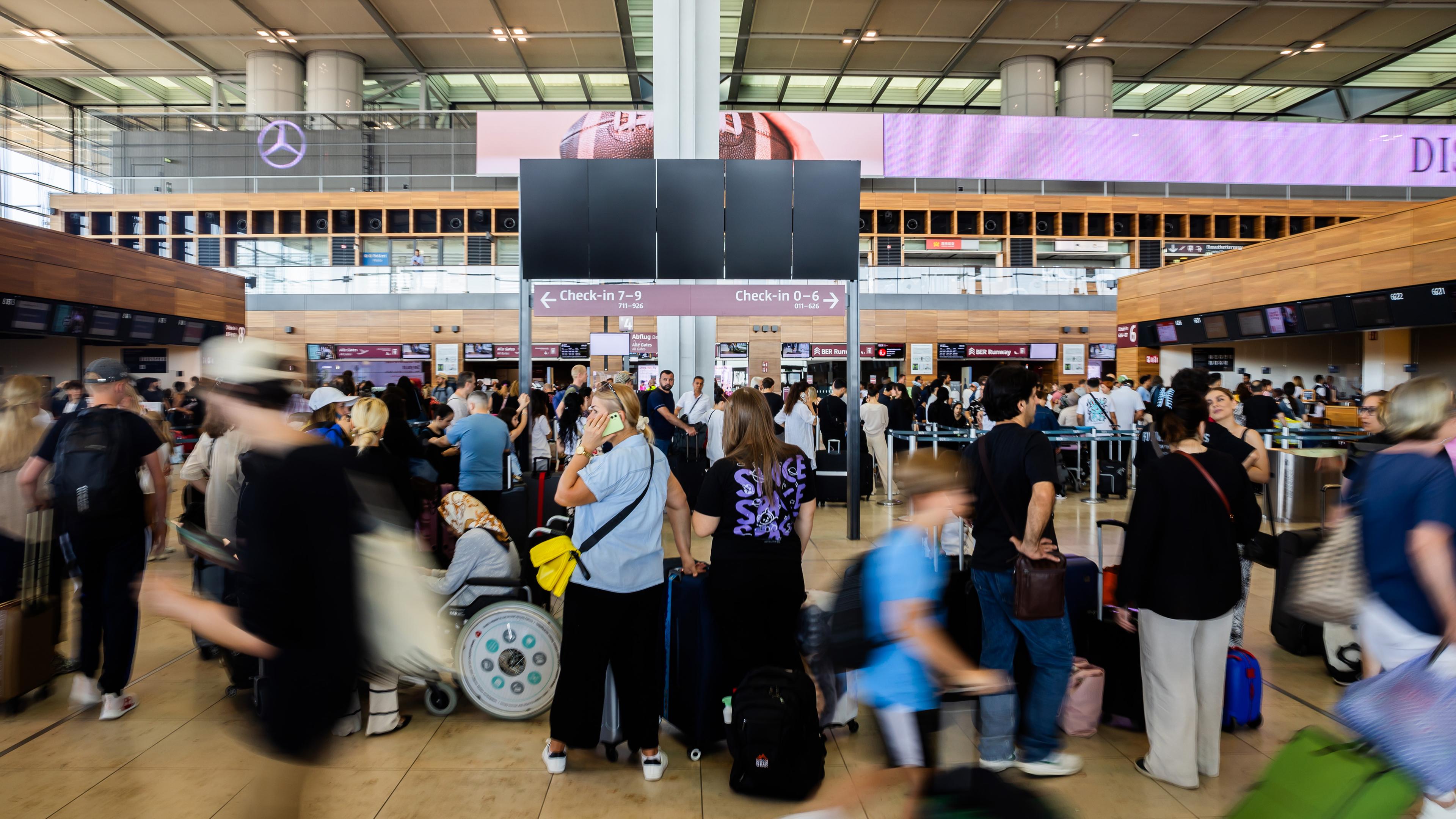  Zahlreiche Fluggäste warten am Hauptstadtflughafen BER vor einer schwarzen Anzeigetafel.