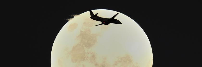 Ein Flugzeug fliegt am Himmel. Im Hintergrund ist der Mond zu sehen. 