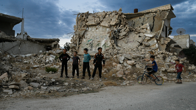 Mehrere Kinder stehen vor einem zerstörten Gebäude in Syrien 