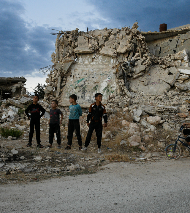 Mehrere Kinder stehen vor einem zerstörten Gebäude in Syrien 