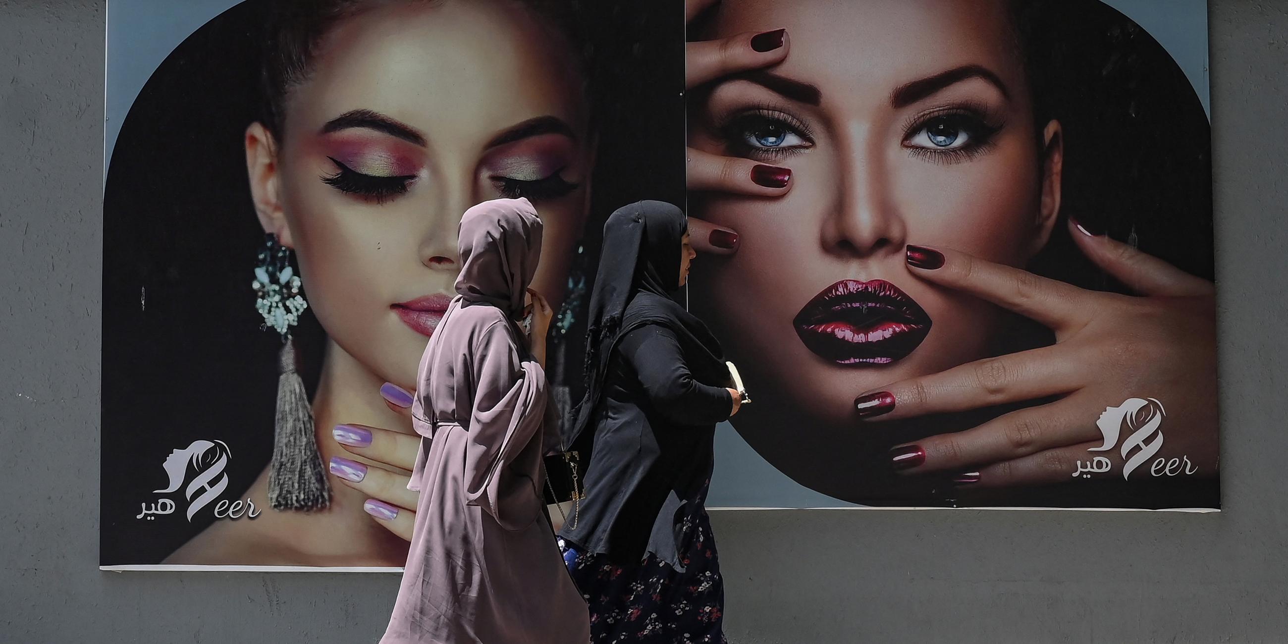 Afghanische Frauen laufen an einer Werbetafel vorbei