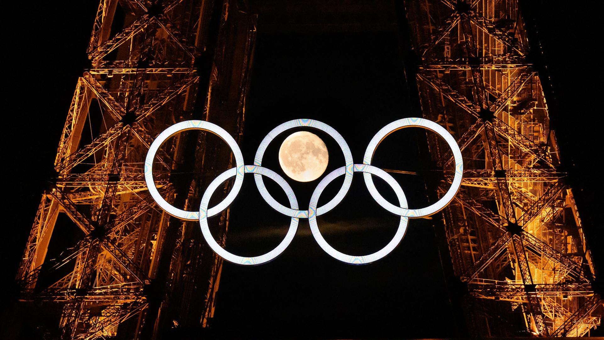 Die Olympischen Ringe am Eiffelturm mit dem Mond im Hintergrund