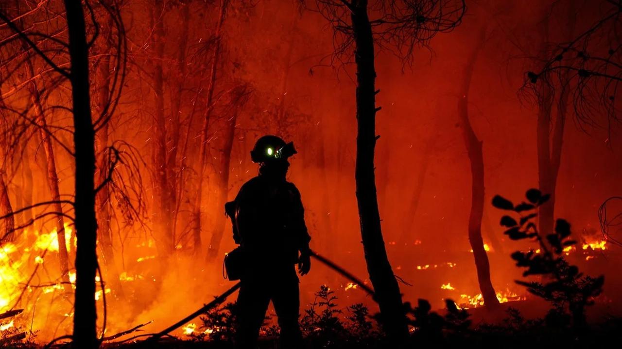 Die Silhouette eines Feuerwehrmannes in einem brennenden Wald.