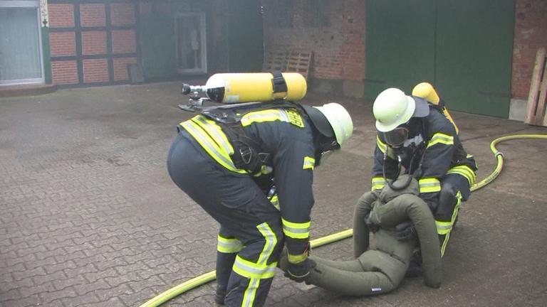 Zwei Feuerwehrleute tragen Puppe weg