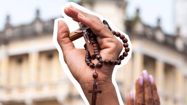 Hand ist in die Luft gestreckt und hält eine Kreuz-Kette in der Hand