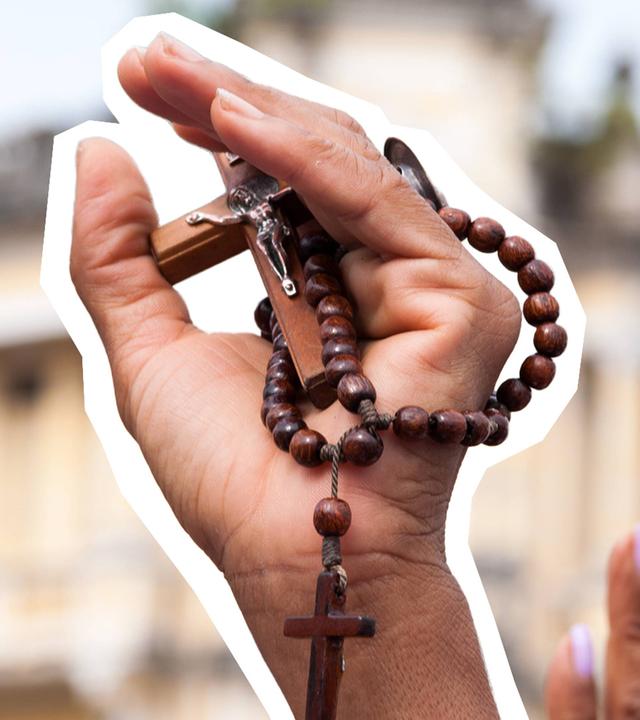 Hand ist in die Luft gestreckt und hält eine Kreuz-Kette in der Hand
