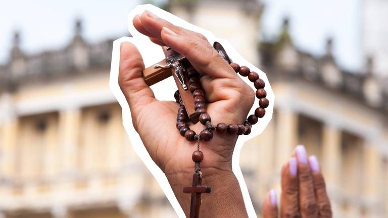 Hand ist in die Luft gestreckt und hält eine Kreuz-Kette in der Hand