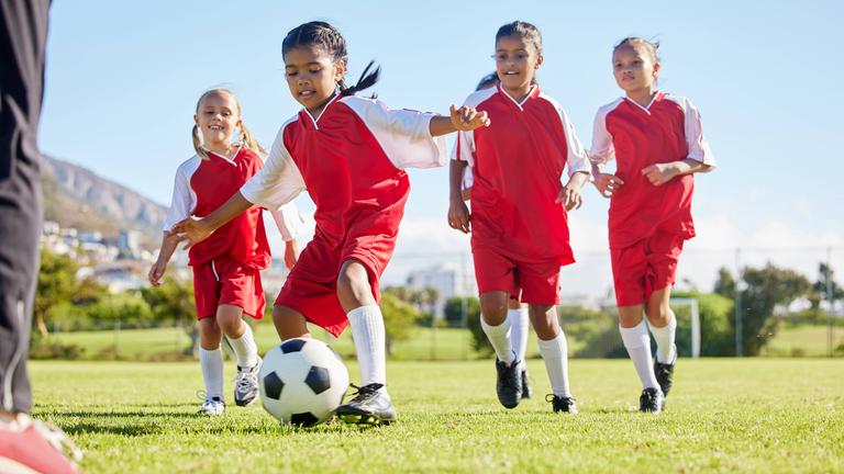 Kleine Mädchen spielen auf dem Rasen Fußball