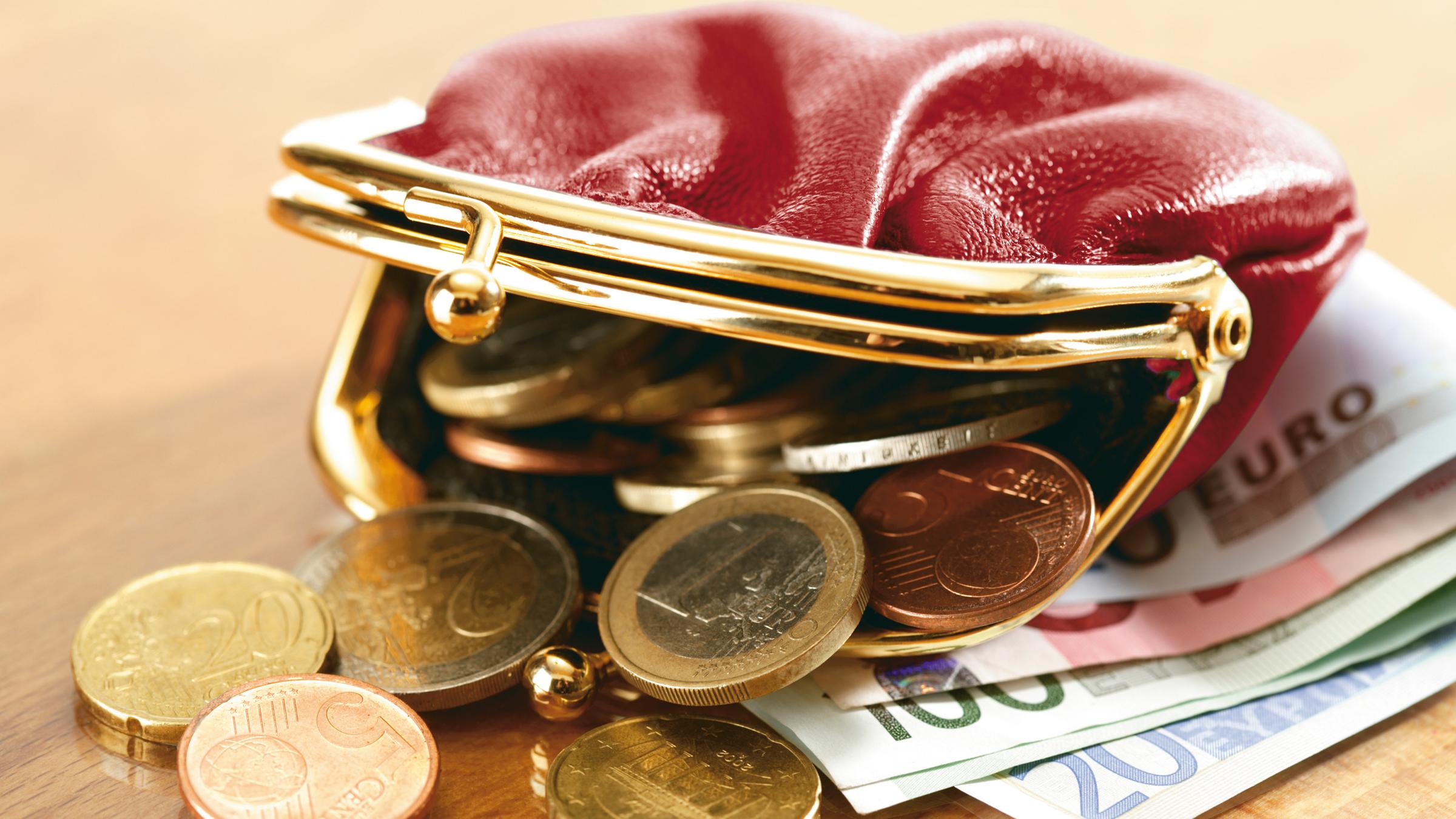 Eine offene Geldbörse, aus der Geld quilt.