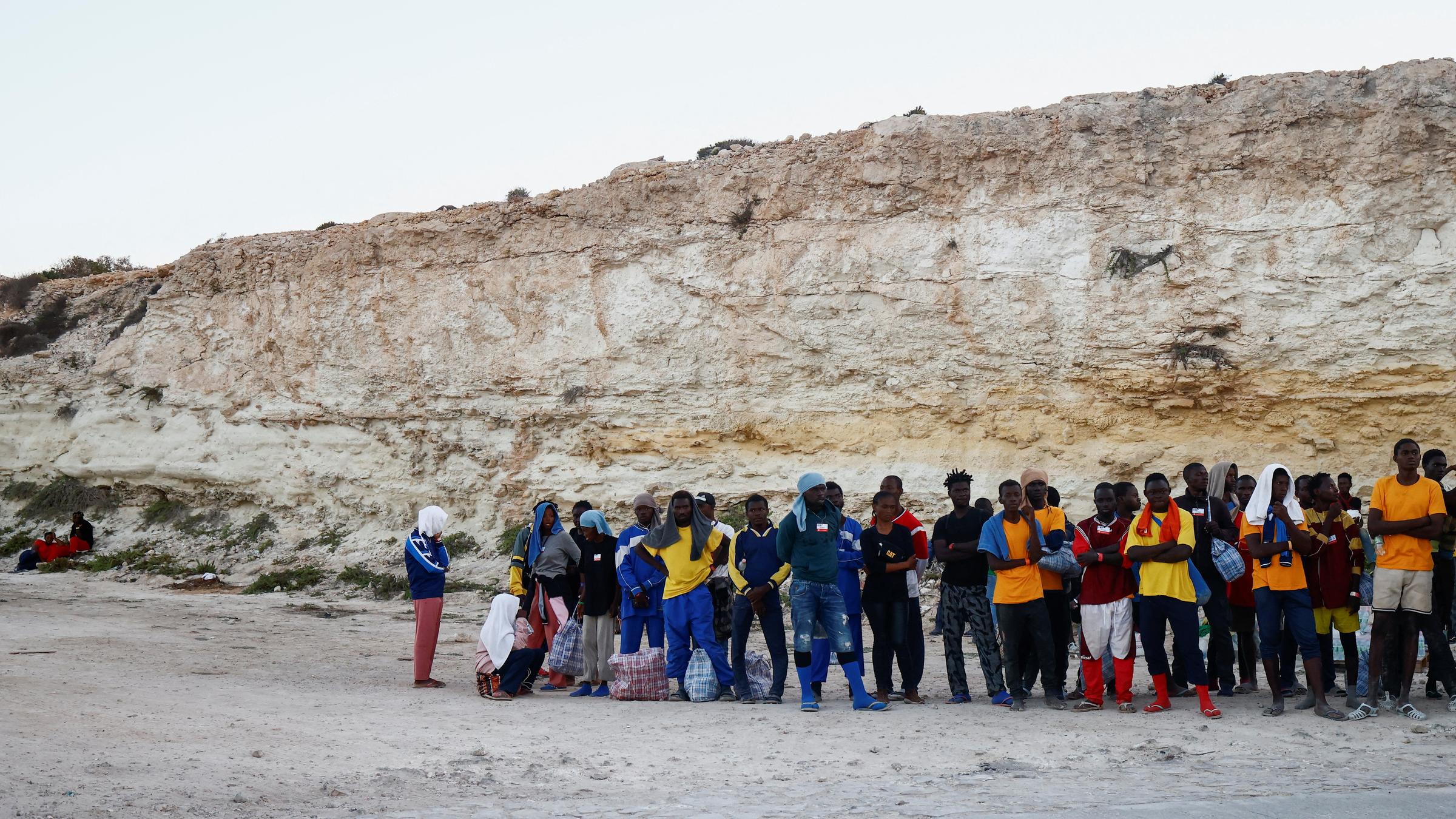 Eine Gruppe Geflüchteter steht wartend am Hafen. 