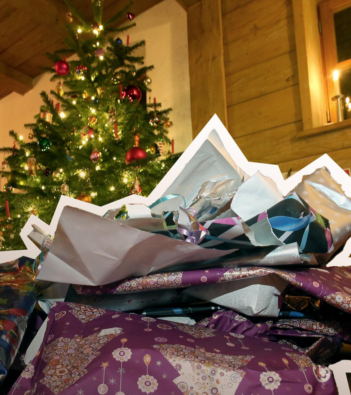 Zerknülltes weihnachtliches Geschenkpapier liegt vor einem geschmücktem Christbaum