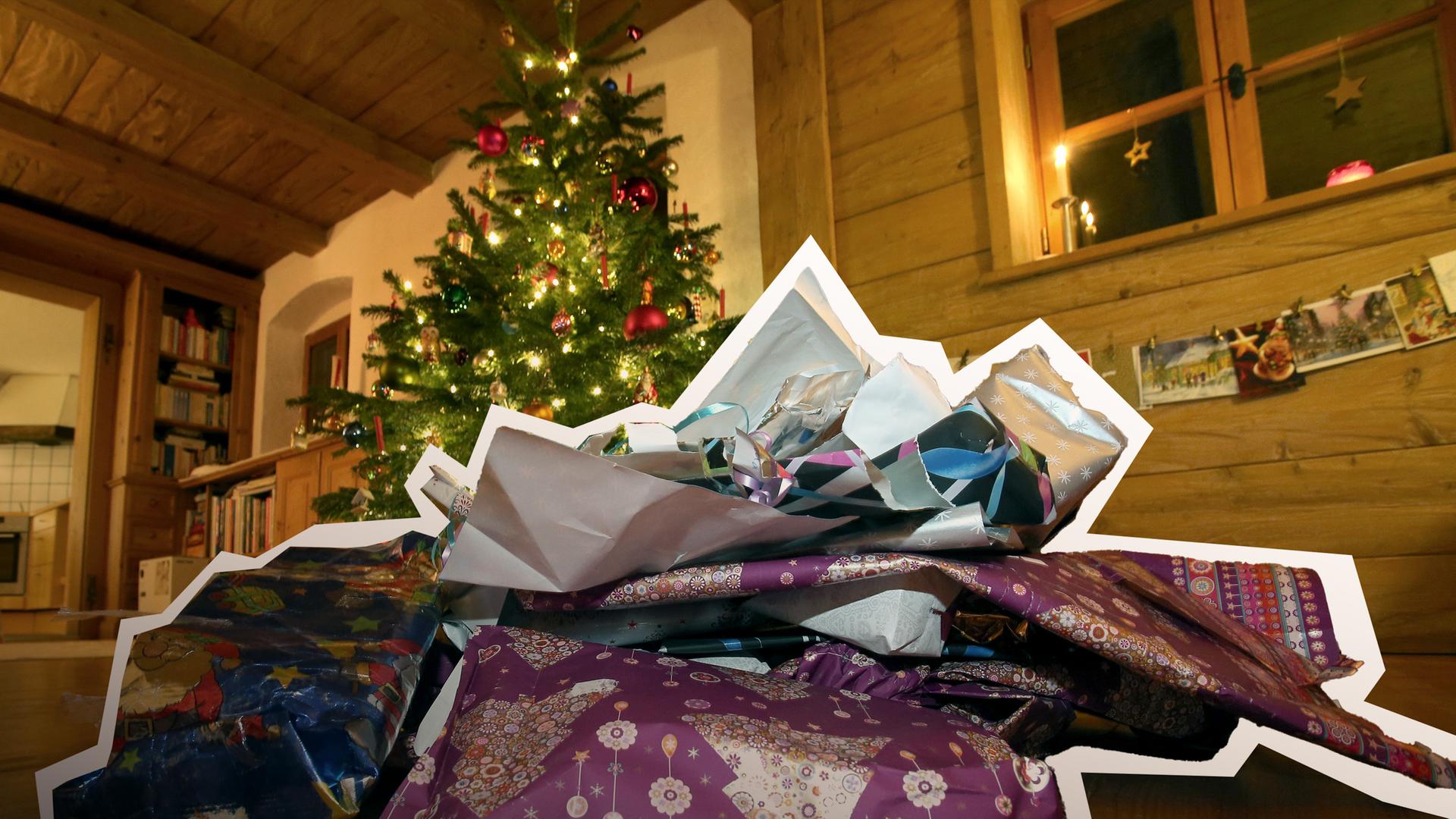 Zerknülltes weihnachtliches Geschenkpapier liegt vor einem geschmücktem Christbaum