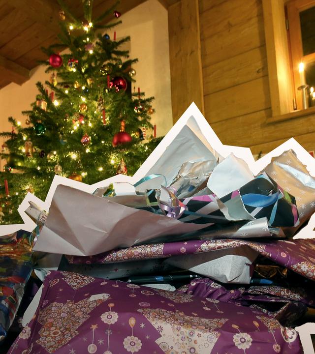 Zerknülltes weihnachtliches Geschenkpapier liegt vor einem geschmücktem Christbaum