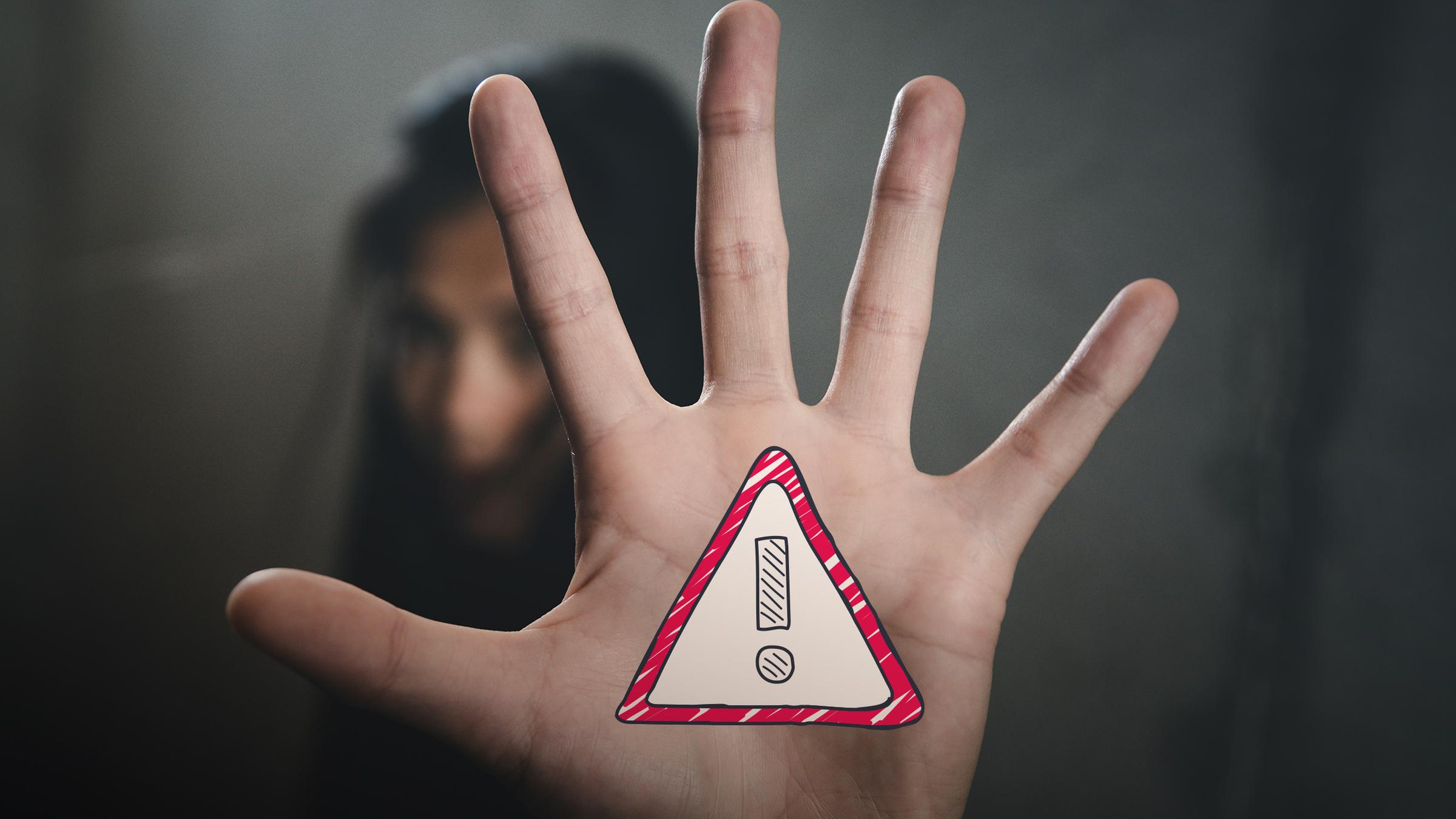 Mädchen unscharf im Hintergrund, im Vordergrund ist ihr abwehrende Hand zu sehen - darauf "Achtung"-Verkehrsschild