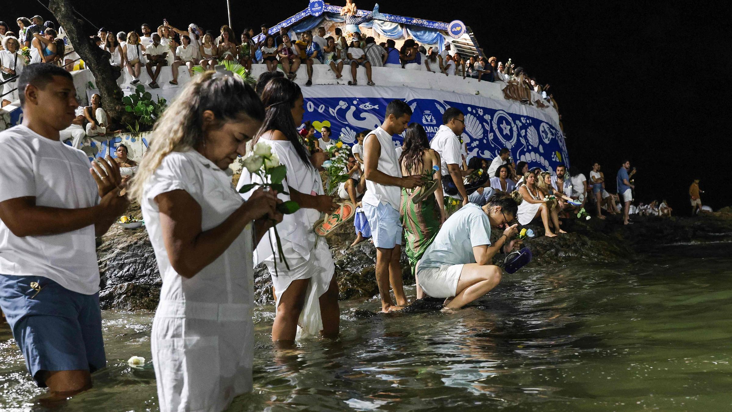 Gläubige stehen am 2. Februar in Salvador mit kleinen Geschenken, Kerzen und Blumen im flachen Wasser im Meer. Sie möchten damit für Schutz, Glück und Segen für das Jahr bitten. 
