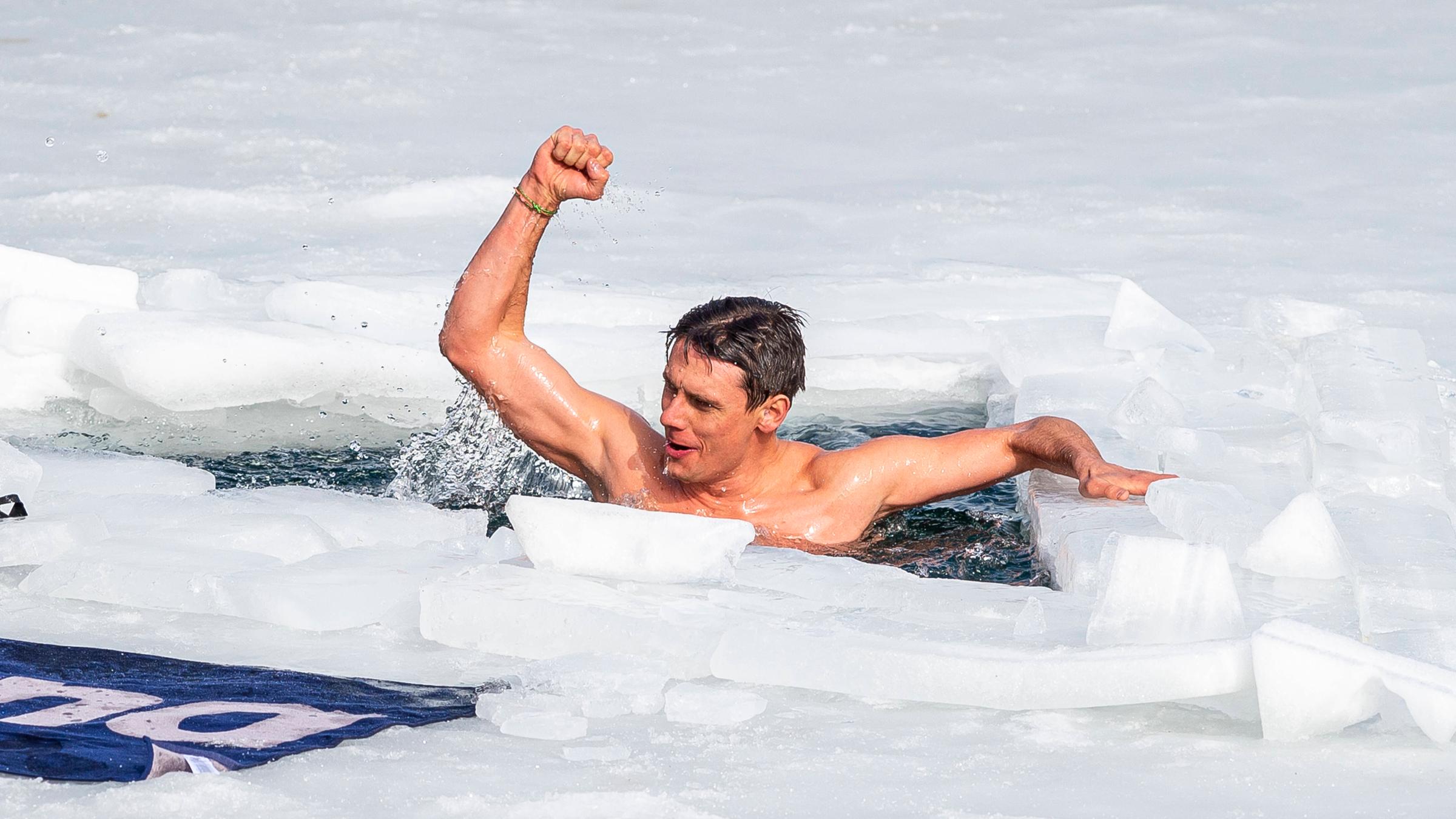 Ein Mann streckt stolz die Hand nach oben. Er schwimmt oberkörperfrei in Eiswasser.