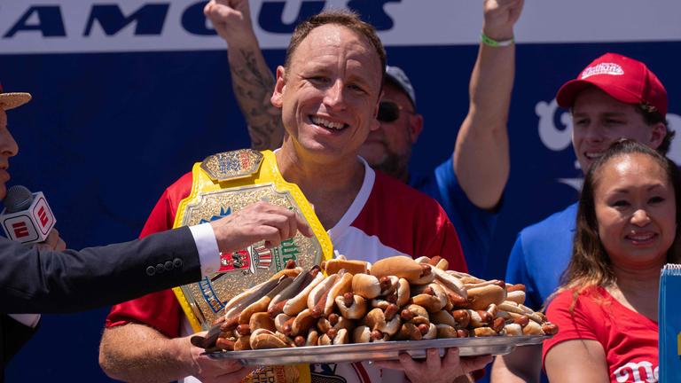 Ein Mann hält einen großen Teller voll Hotdogs in den Händen.