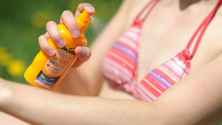 junge frau sprueht sich mit sonnencreme ein