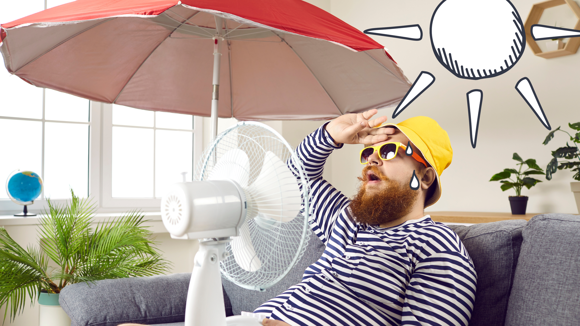 Ein Mann sitzt mit Ventilator auf der Couch, er trägt einen Hut, eine Sonnenbrille. Im Hintergrund ist ein Sonnenschirm 