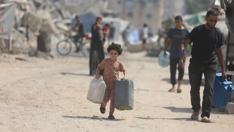 Ein kleines Mädchen trägt zwei Wasserkanister. 