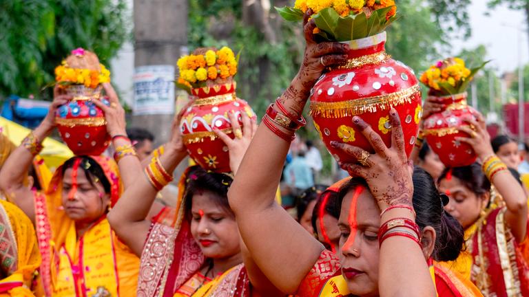 Hindu-Frauen in orangen Gewändern tragen Wasser in Krügen auf ihren Köpfen. 