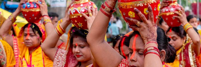 Hindu-Frauen in orangen Gewändern tragen Wasser in Krügen auf ihren Köpfen. 