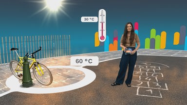 Teresa steht im logo!-Studio, neben ihr ein Thermometer, das 30 und 60 Grad anzeigt, daneben ein gelbes Fahrrad und ein Stück Straßenbelag, auf dem mit Kreide gemalt wurde.