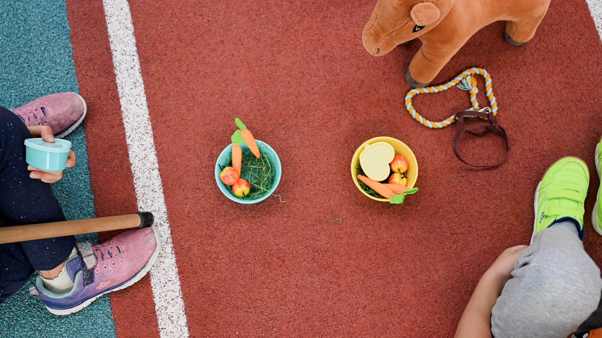 Menschen sitzen auf dem Boden, es sind Schüsseln mit Spiel-Essen zu sehen. 