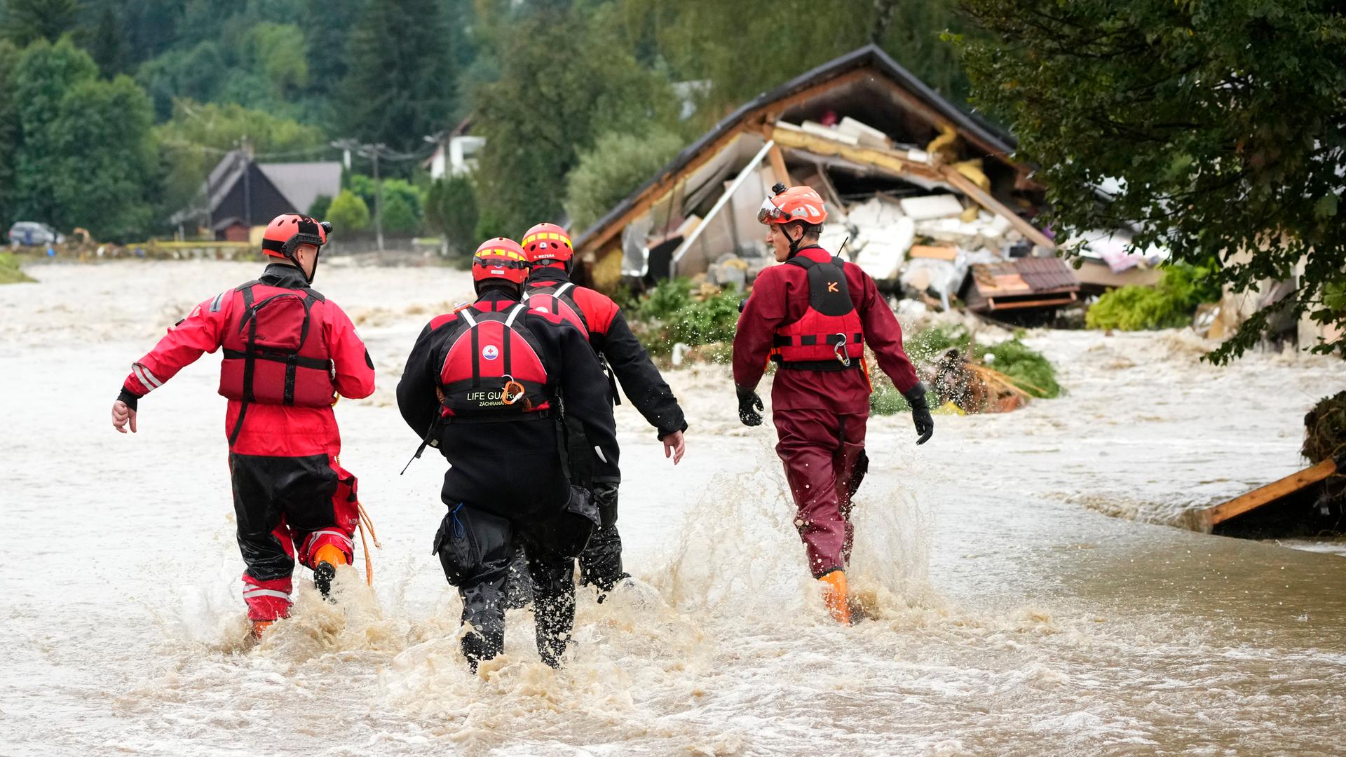 Vier Feuerwehrleute gehen durch eine überflutete Straße.