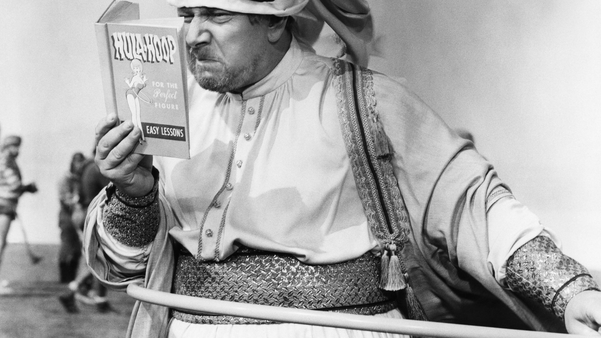 Ein König hat einen Hula-Hoop-Reifen um und schaut dabei kritisch in eine Anleitung