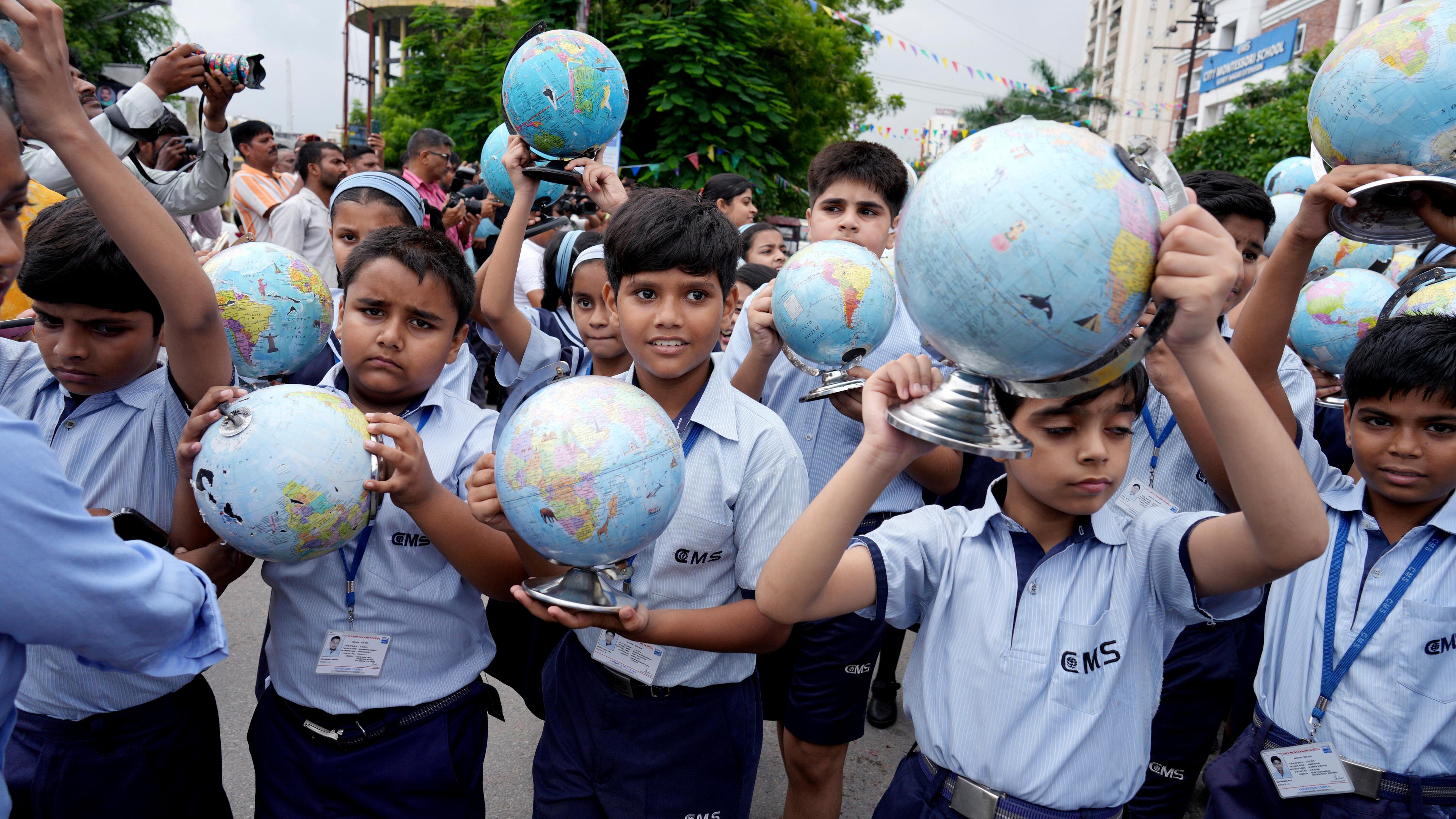 Mehrere Kinder halten bei der Rückkehr des Astronauten Shubhanshu Shukla auf die Erde Globen in die Luft.