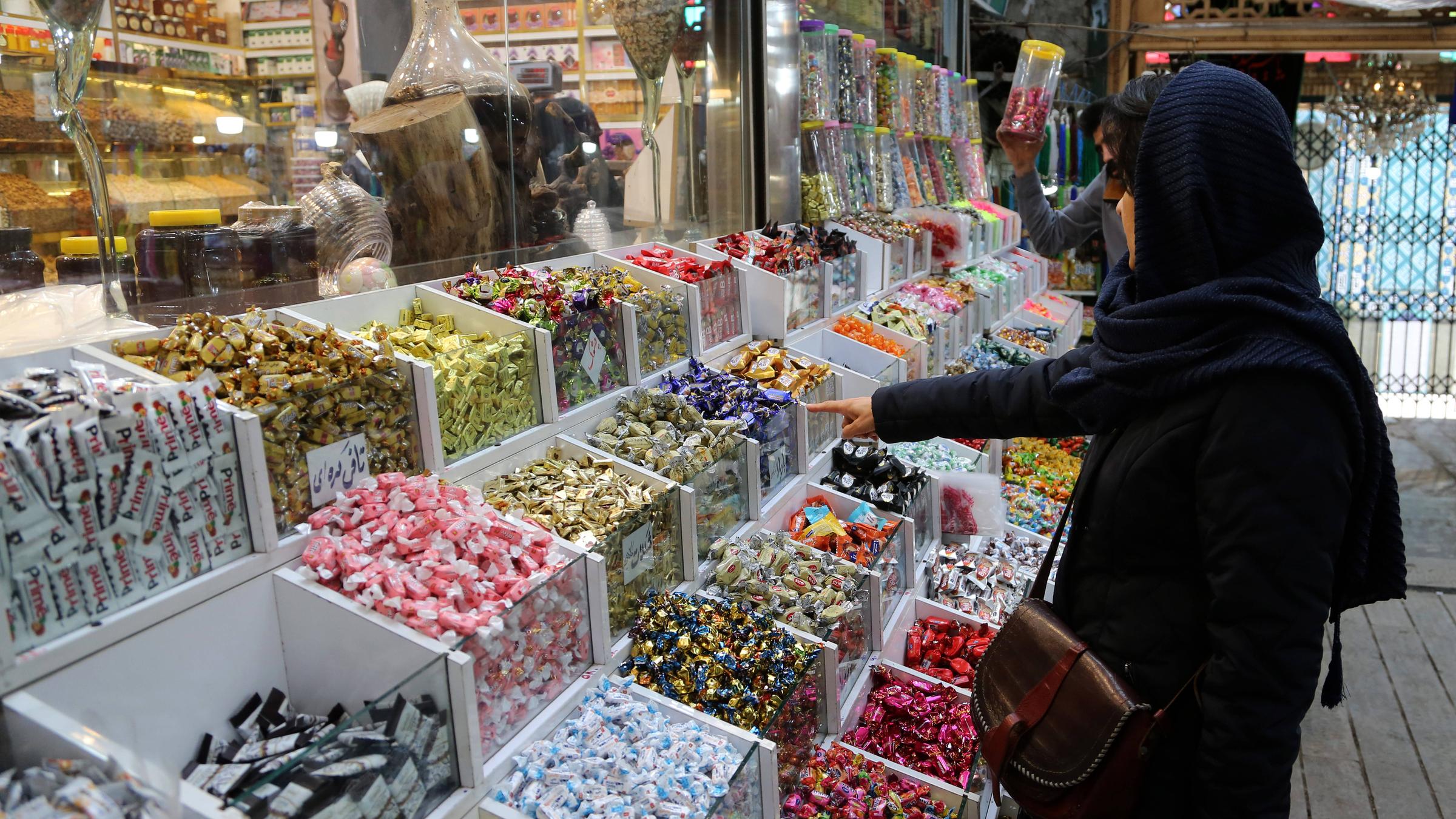 Frau in Iran in Einkaufsladen, steht vor Süßigkeitenregal und zeigt mit Finger auf Süßigkeit