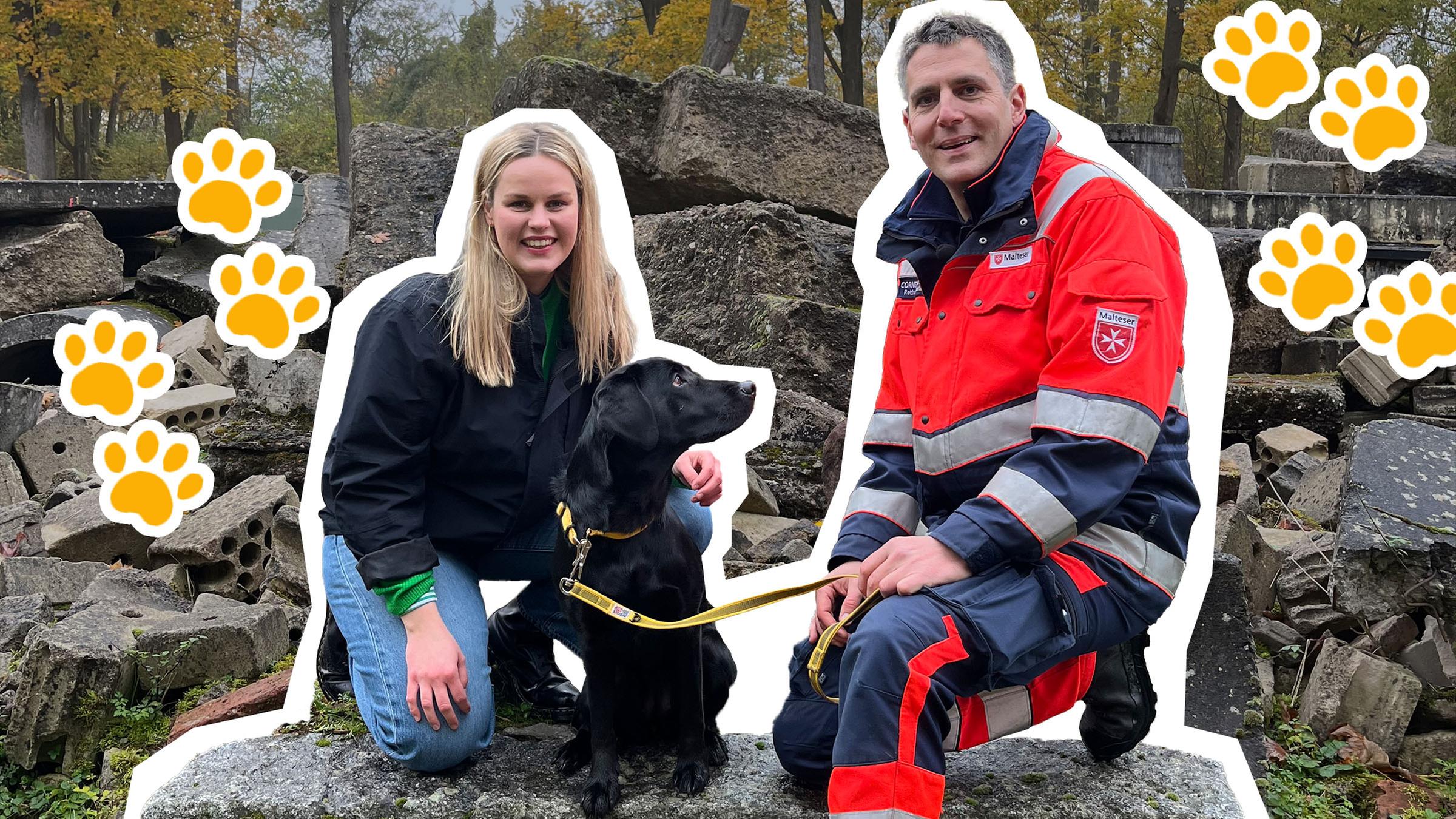 Isabelle und ein Sanitäter hocken auf einem Stein, zwischen ihnen ein schwarzer Hund, daneben Hundepfoten.