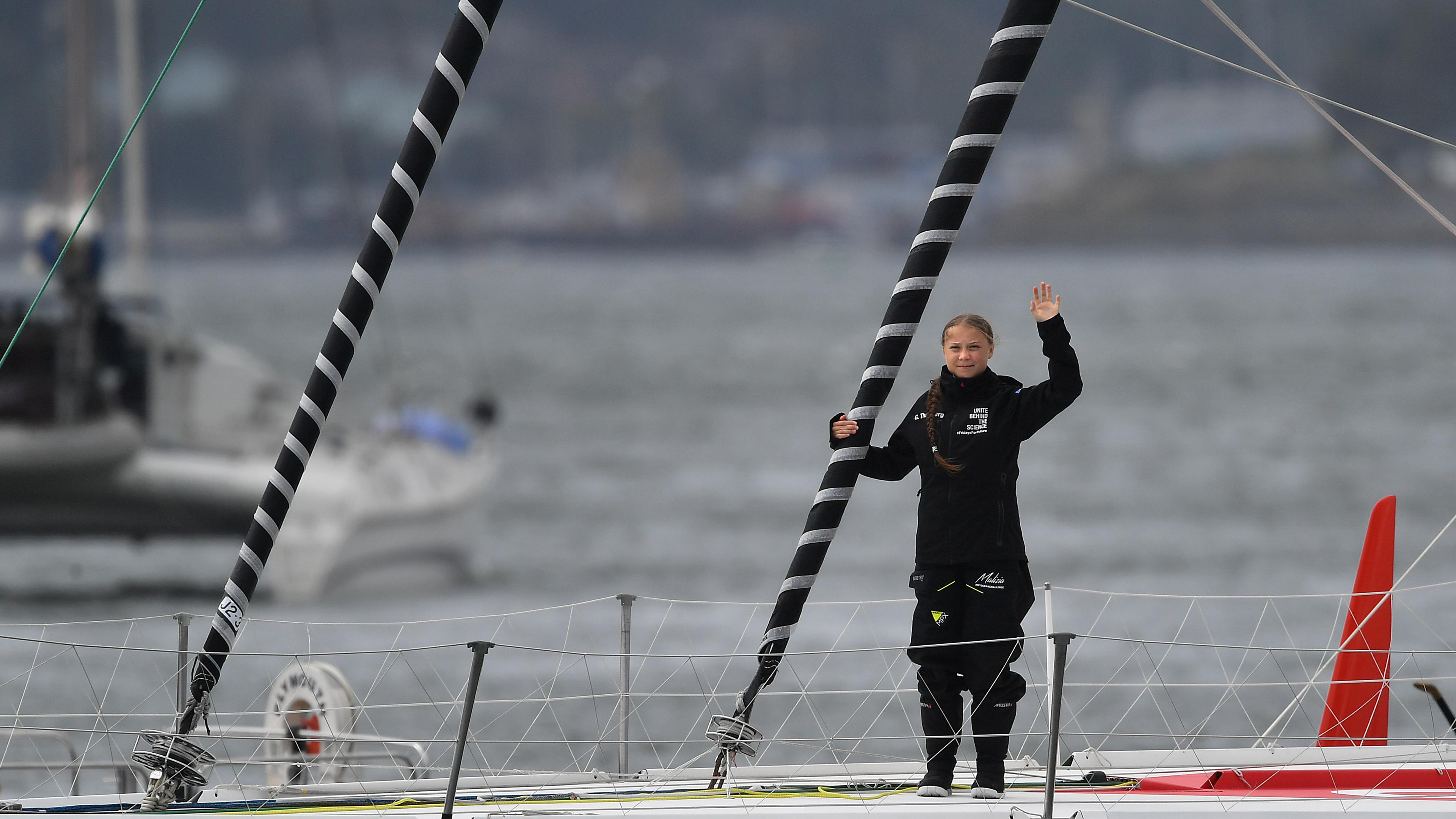 Greta Thunberg steht winkend auf einer Hochseejacht. 
