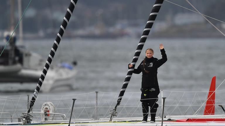 Greta Thunberg steht winkend auf einer Hochseejacht. 